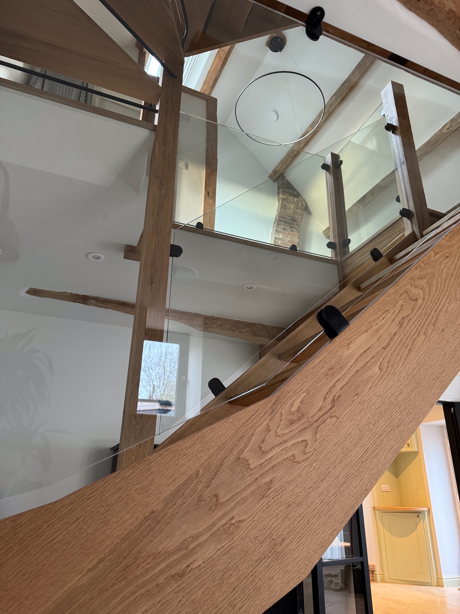 Close up of oak staircase with glass balustrade looking up from ground level to first floor with circular light feature at the top